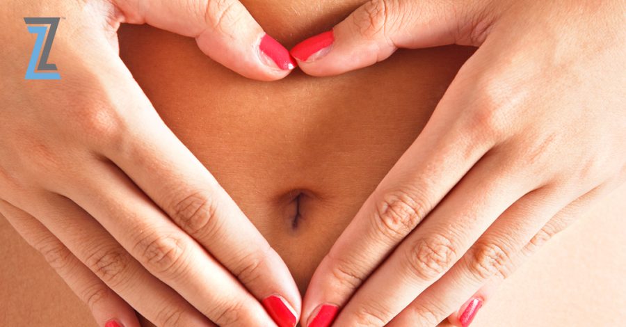 Close-up of a woman's toned abdomen and belly button with her hands forming a heart shape