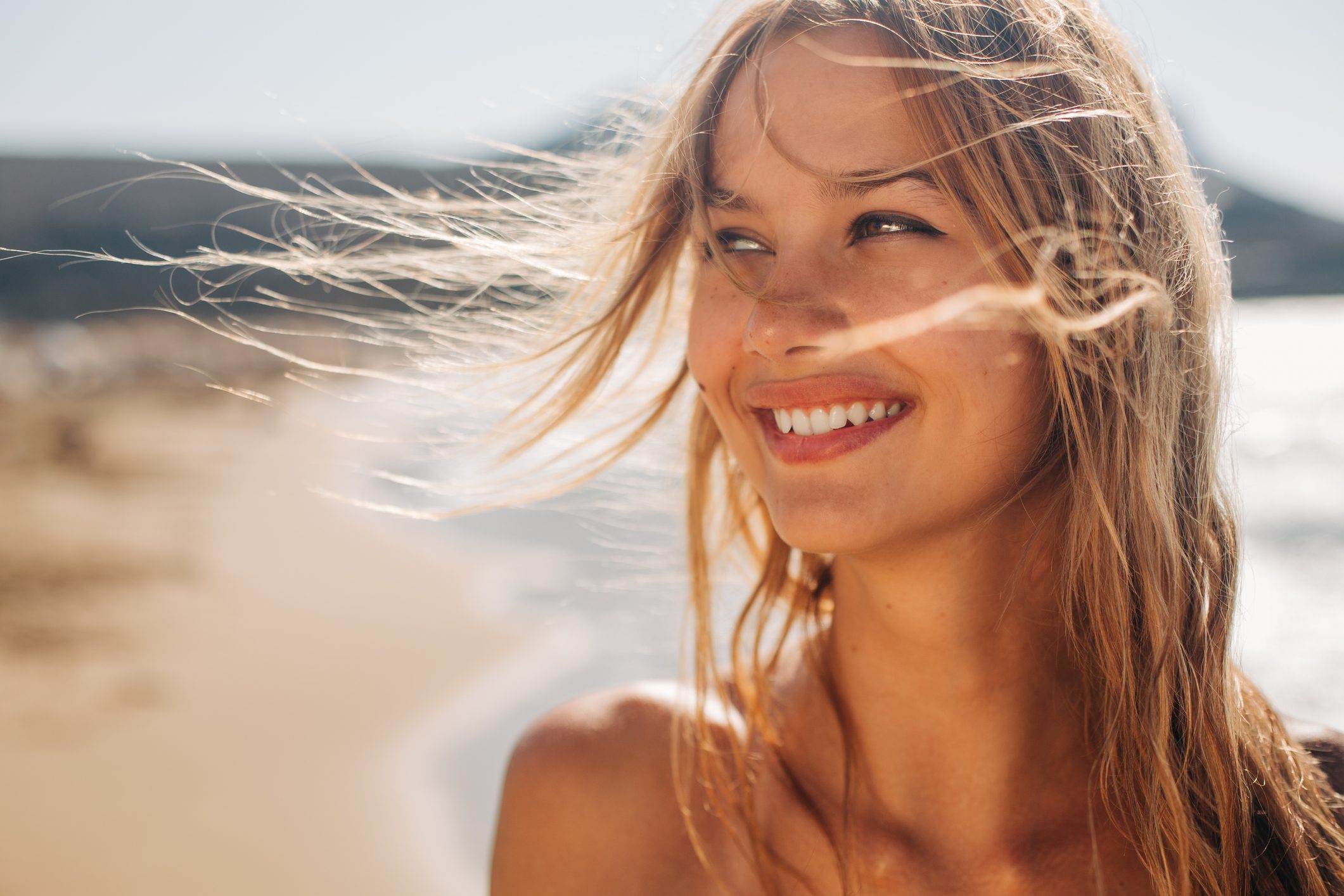 Woman with sun-lit blonde hair smiling outdoors at the beach